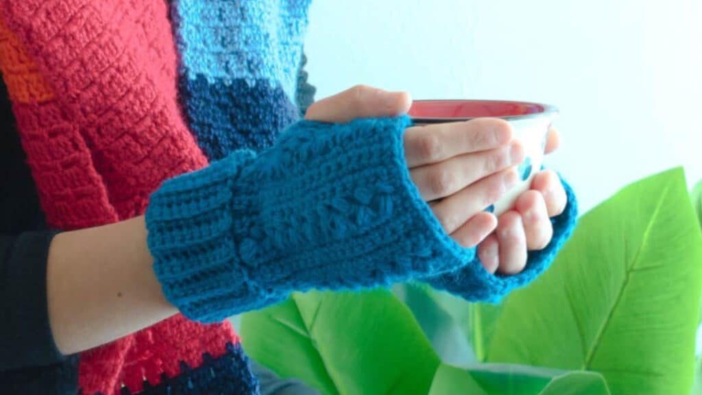 A pair of blue finger less gloves on hands, holding a cup.