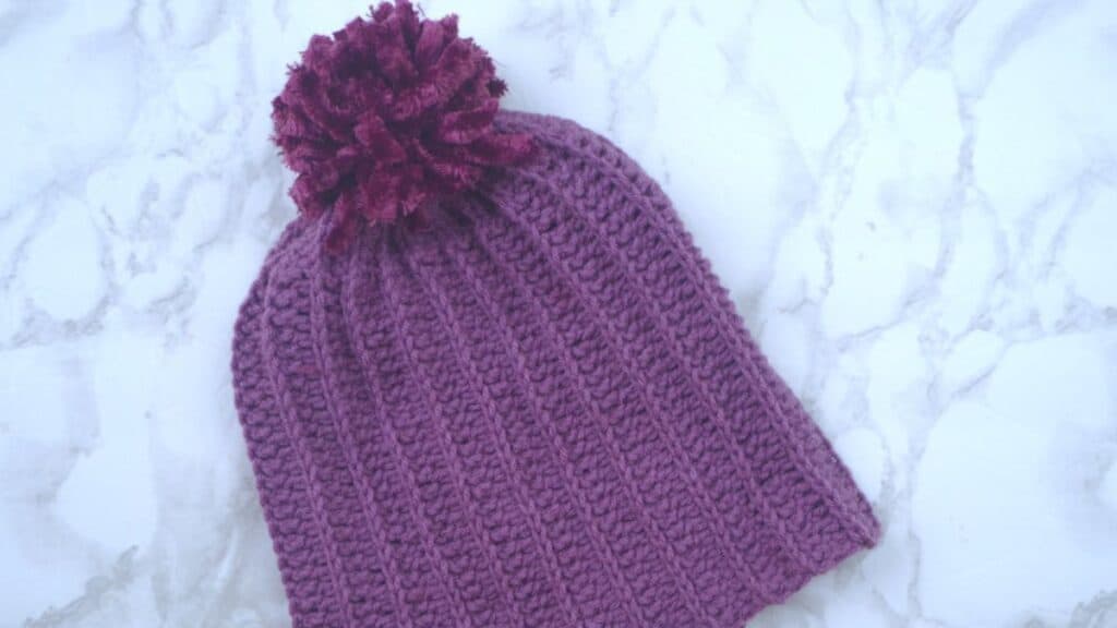 A purple beanie hat with a pom pom top.